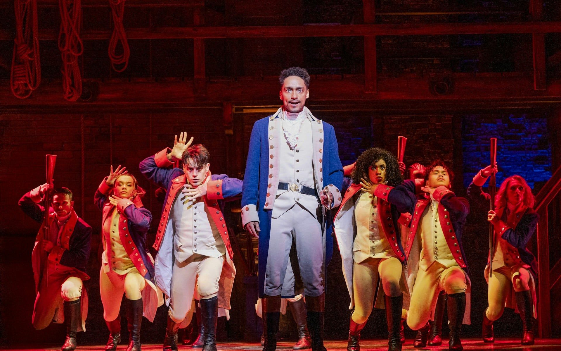 Performers in colonial costumes on stage during a Hamilton musical scene