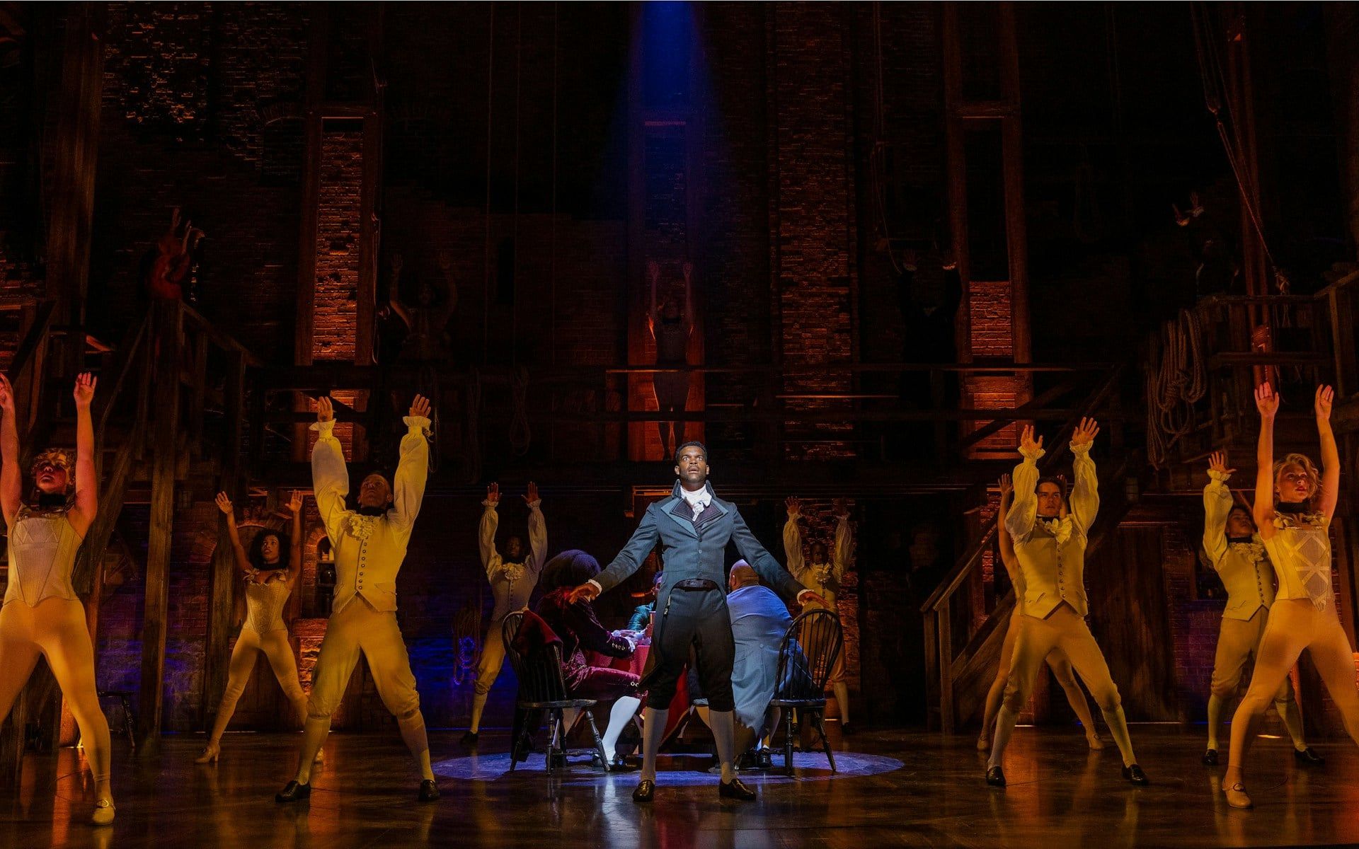 Cast performing a scene from Hamilton on stage with dramatic lighting