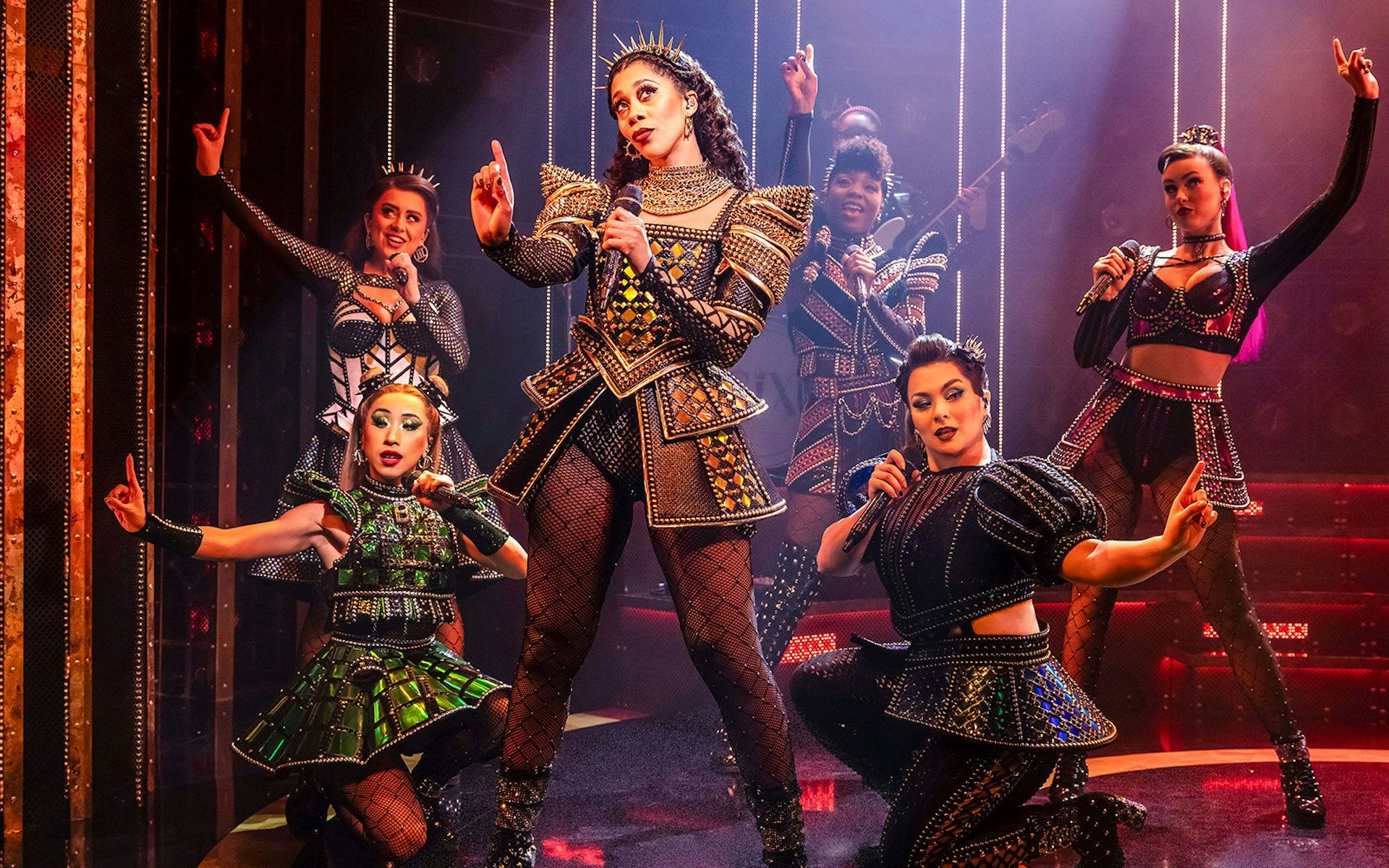 Performers in vibrant costumes on stage during the musical "Six