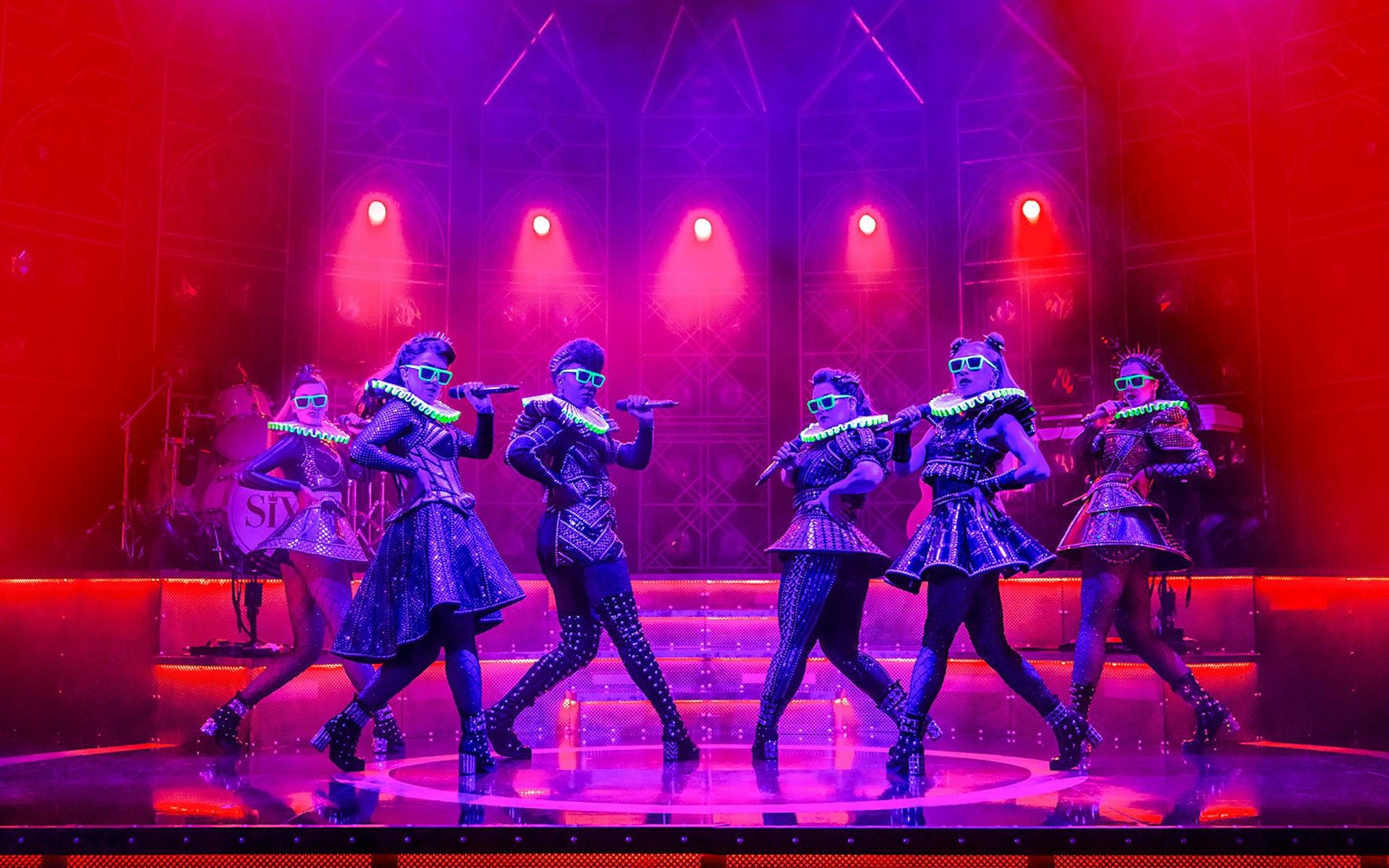 Performers on stage in vibrant costumes during the musical "Six" with dramatic lighting