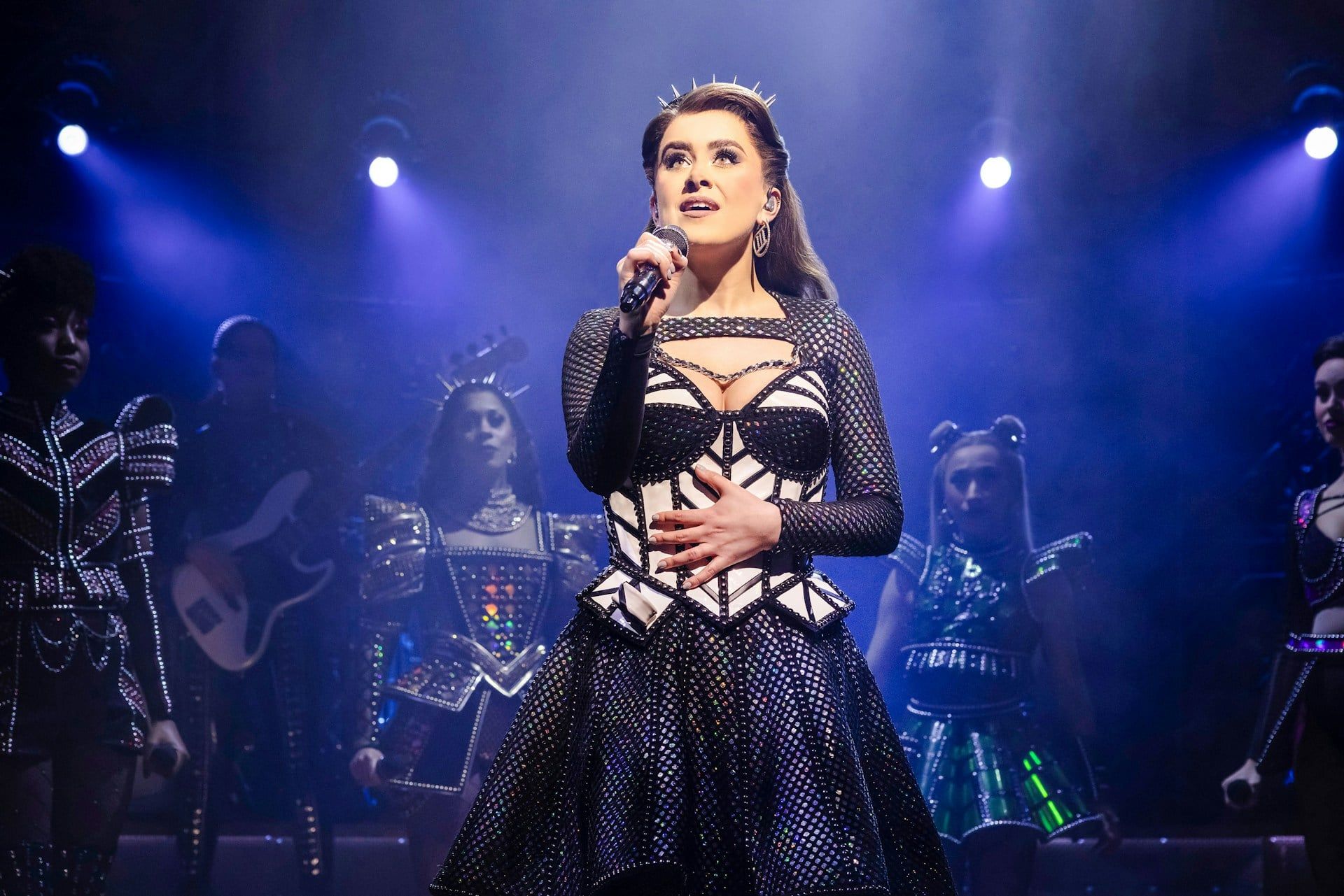 Performer singing on stage during the musical "Six" with a spotlight and backup singers