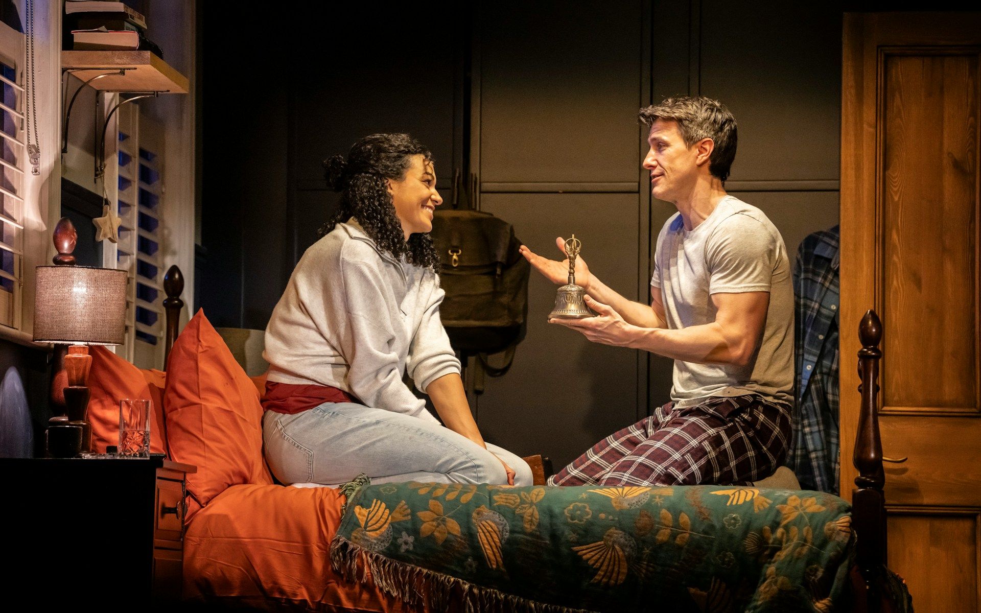 Stage scene from Paranormal Activity, Westend, with two actors on a bed discussing a bell