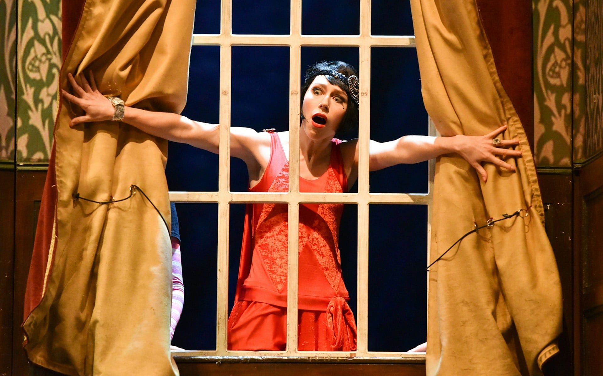Performer in red dress on stage during "The Play That Goes Wrong" scene