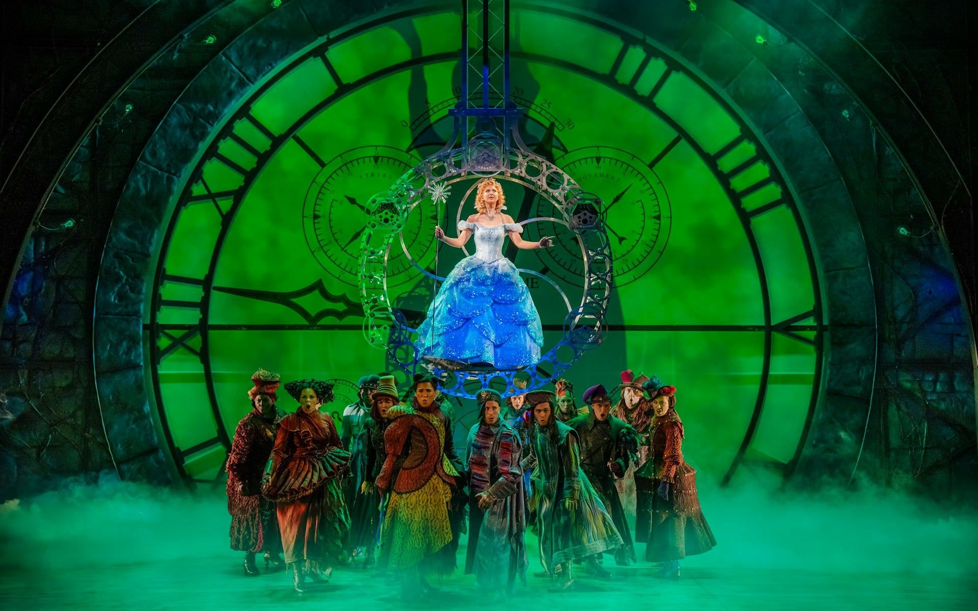 Stage scene from the musical Wicked with performers in front of a large clock