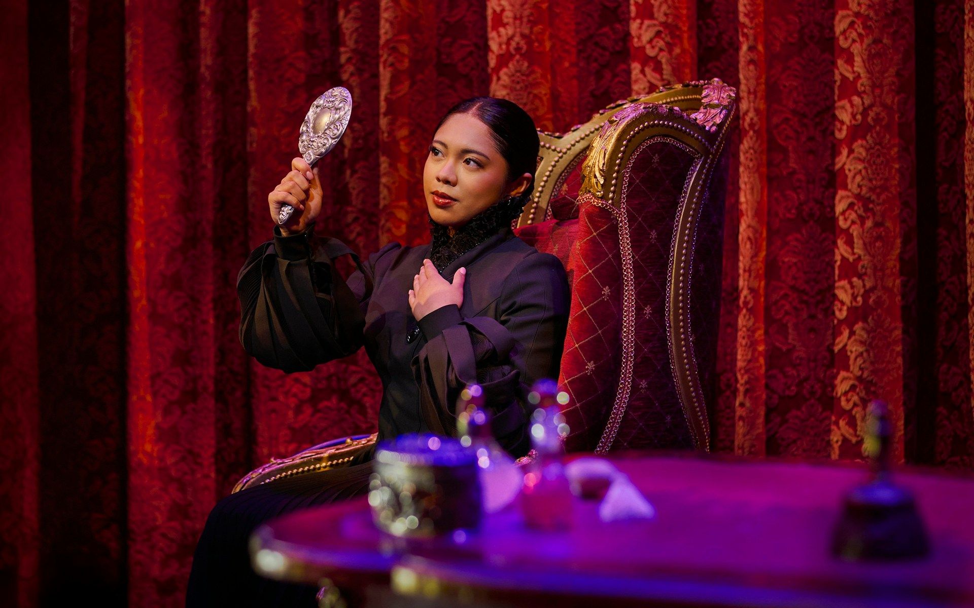 Performer in costume holding a mirror on stage during a scene from Wicked