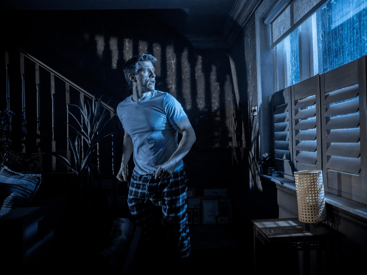 Man in a dimly lit room looking out a window during Paranormal Activity stage performance, Westend