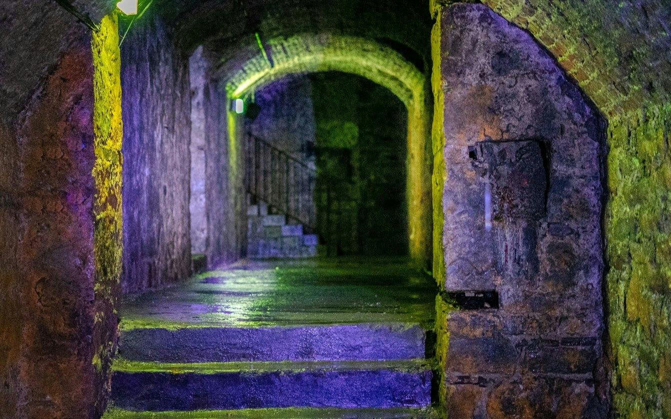 Dimly lit stone corridor in Edinburgh's Terror Tour with arched ceiling and stairs.