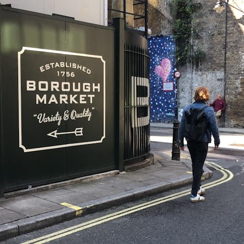 A person walks past a green sign for Borough Market, with surrounding buildings and bystanders in the background.