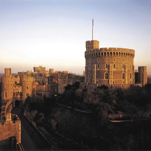 A large medieval castle with multiple towers and battlements under a clear sky at dusk, highlighted with warm, golden light.
