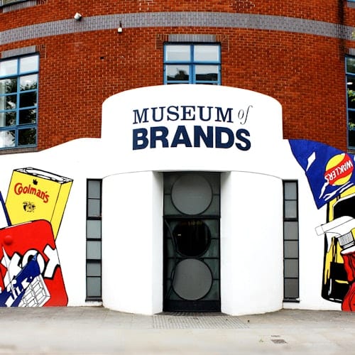 Brick building facade with "Museum of Brands" signage above entrance, surrounded by colorful graphics of branded products.