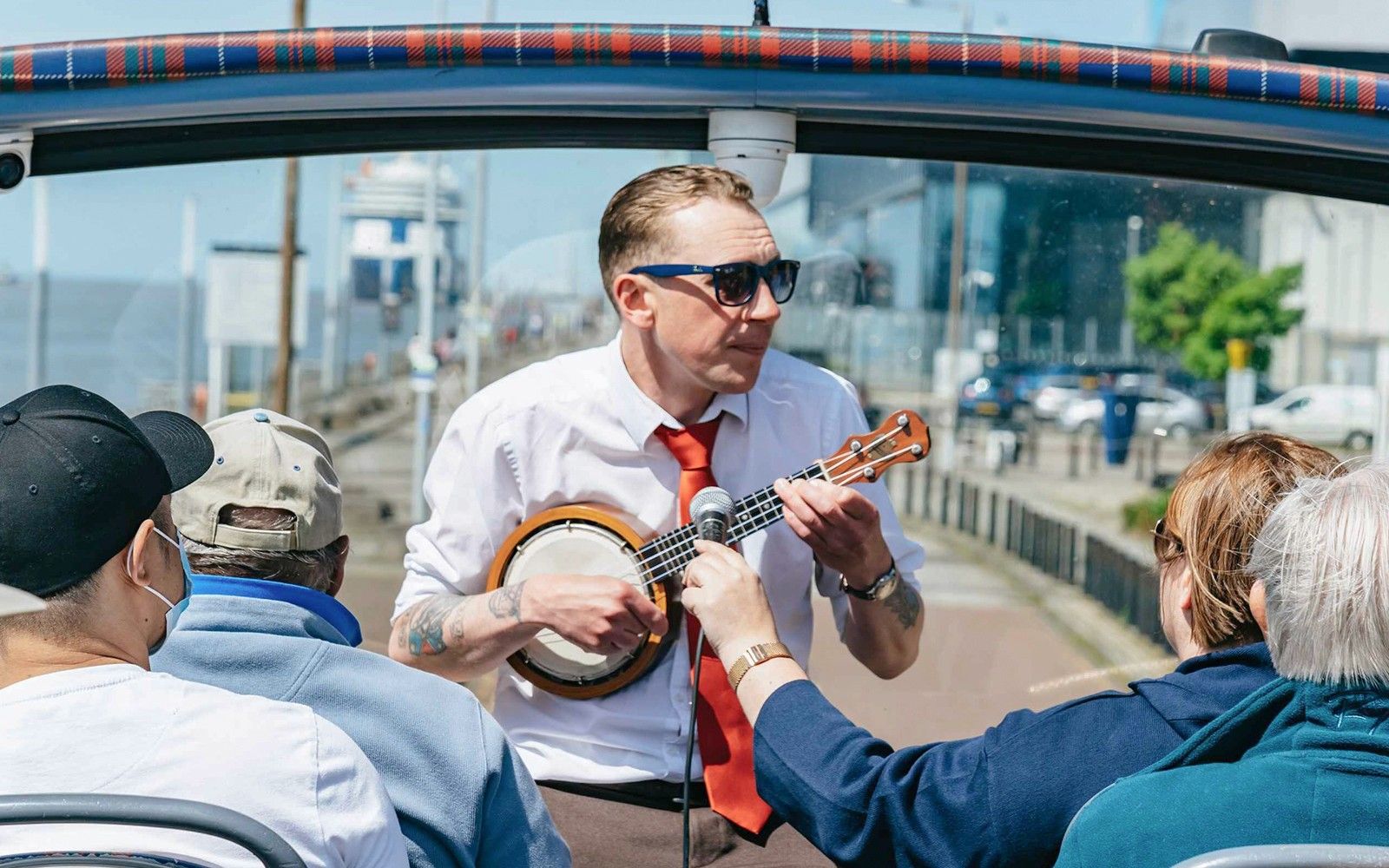Guide playing banjo on Liverpool hop-on hop-off city and Beatles tour.