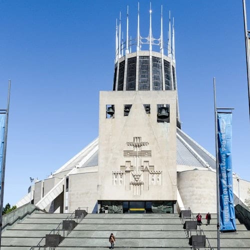 Modern cathedral with a distinctive central tower, large staircase in front, and blue banners on either side. Clear blue sky.