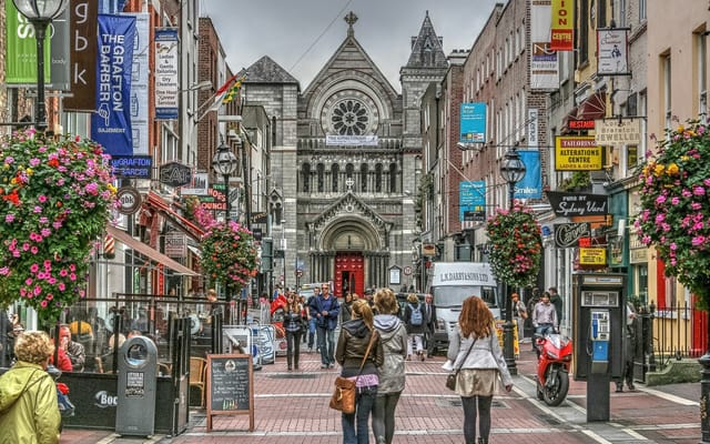 Pedestrians on a bustling street in Dublin with a historic church in the background.